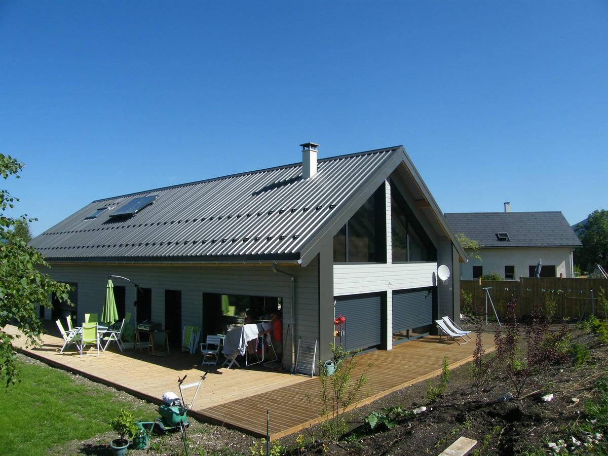La maison terminée : bardage gris, toiture à deux pans et terrasse en bois.