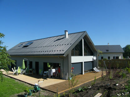 La maison terminée : bardage gris, toiture à deux pans et terrasse en bois.